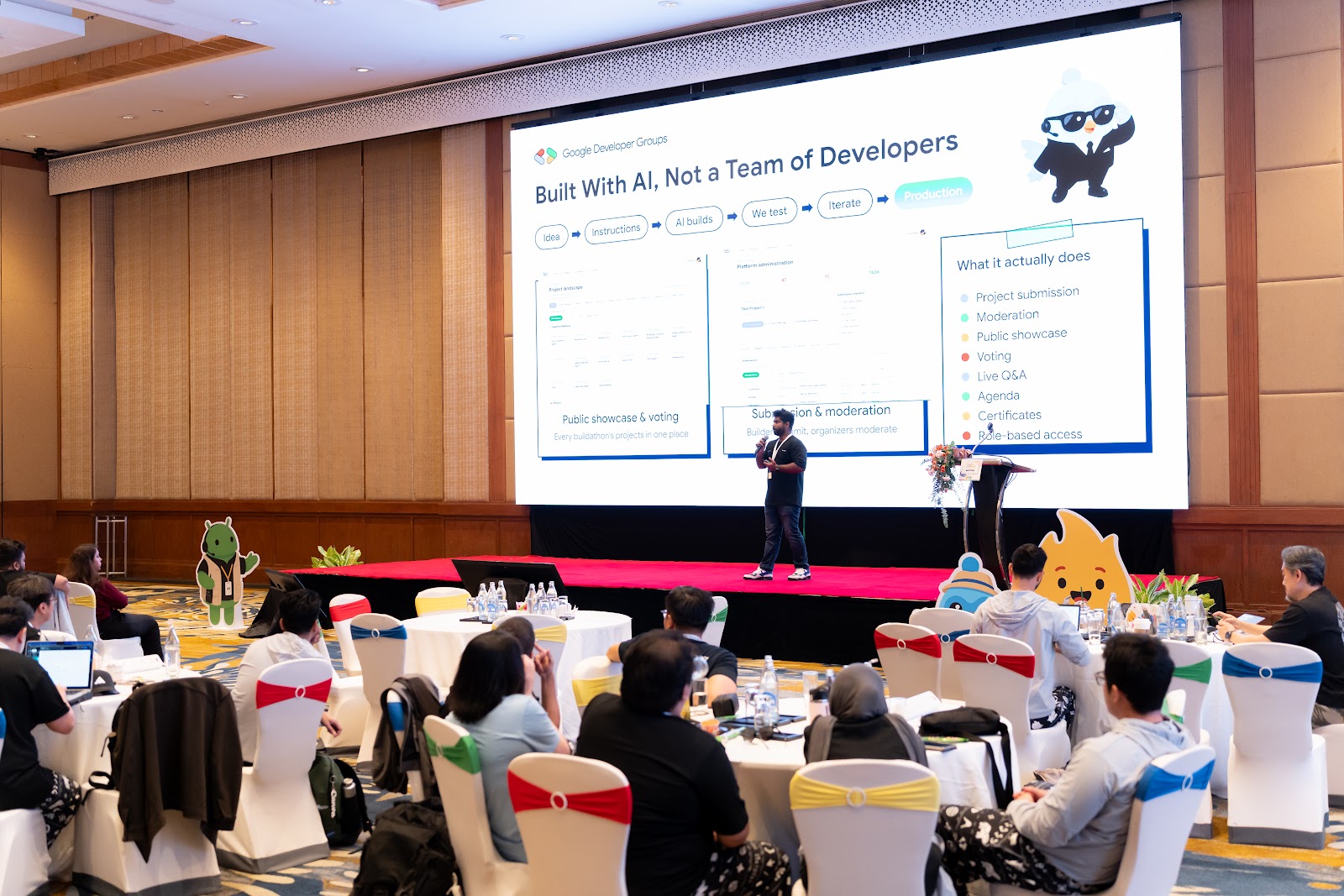 Wide shot of the Built With AI, Not a Team of Developers slide on stage, showing the build loop and the platform's feature list
